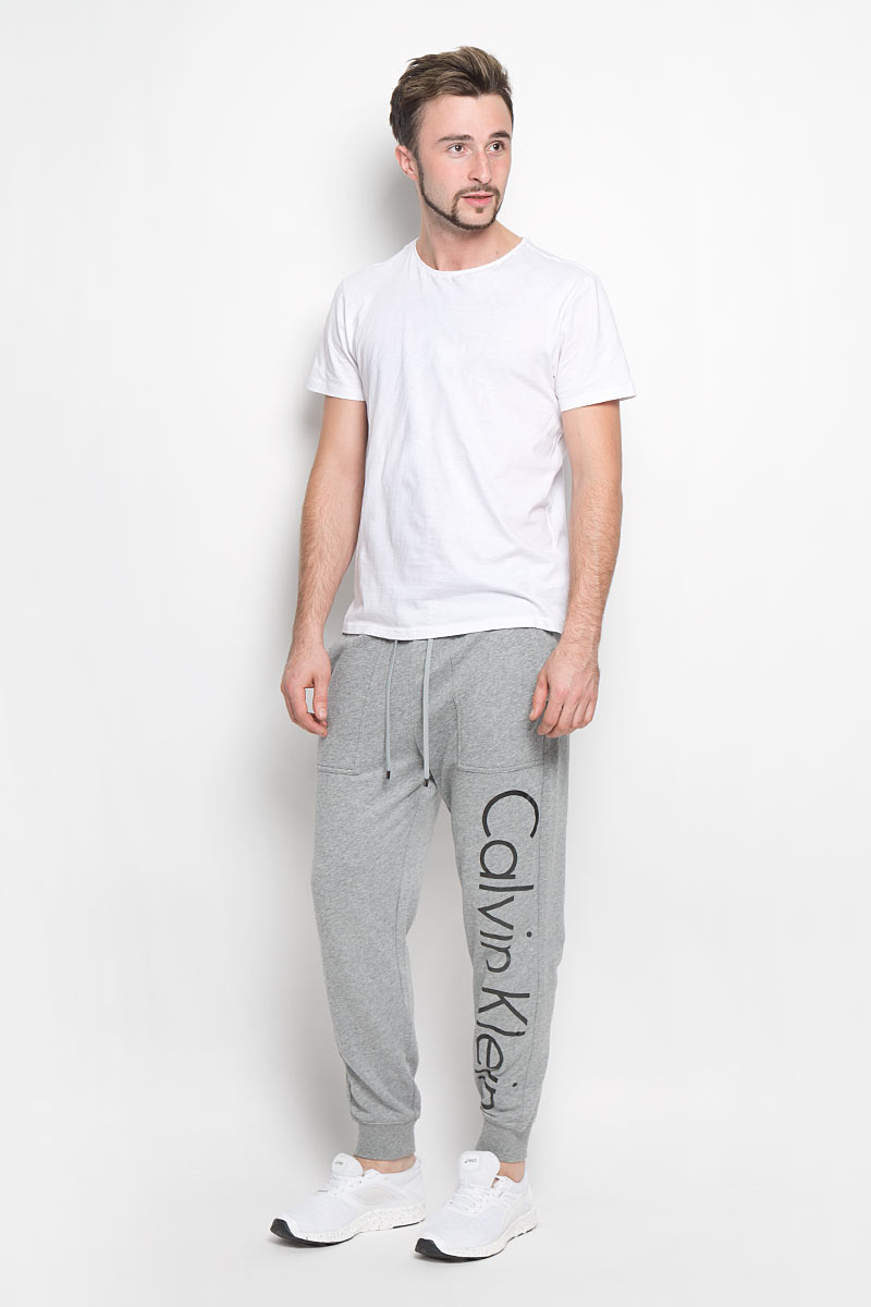 Брюки для дома мужские Calvin Klein Underwear, цвет: серый. NM1263E. Размер XL (54)NM1263E_2GY Брюки для дома мужские Calvin Klein Underwear, цвет: серый. NM1263E. Размер XL (54)NM1263E_2GYМужские брюки для дома Calvin Klein Underwear выполнены из хлопка с добавлением полиэстера. Изнаночная сторона изделия с теплым начесом. Эластичный пояс с затягивающимся шнурком позволяет отрегулировать посадку точно по фигуре. Спереди расположены два втачных кармана. Низ брючин дополнен трикотажными манжетами. Оформлено изделие термоаппликацией в виде надписи.